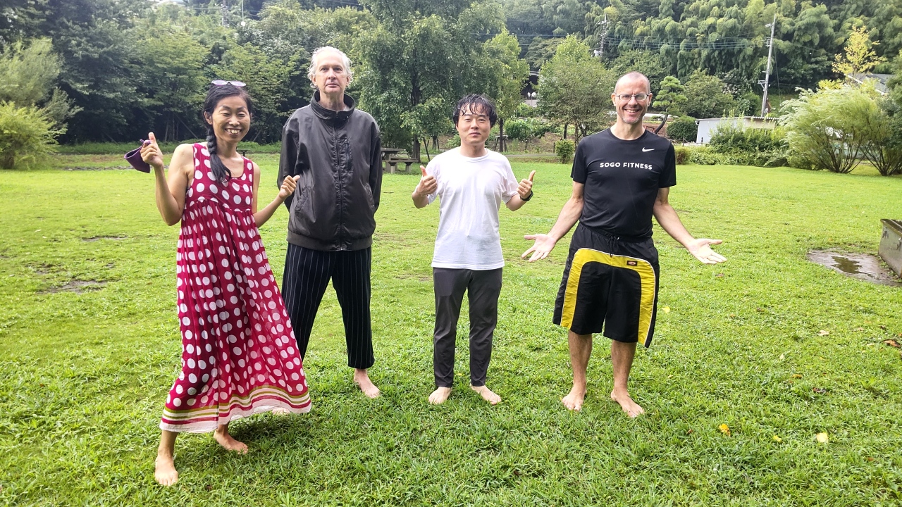 Four barefoot adults standing in grass and rain, happily posing without masks